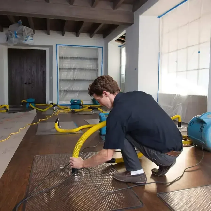 Technician on a hardwood floor with yellow hosing, drying mats and air movers around him