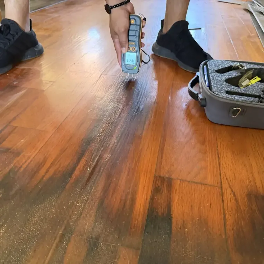 Moisture meter being used on a glossy hardwood floor to check how far the water has spread