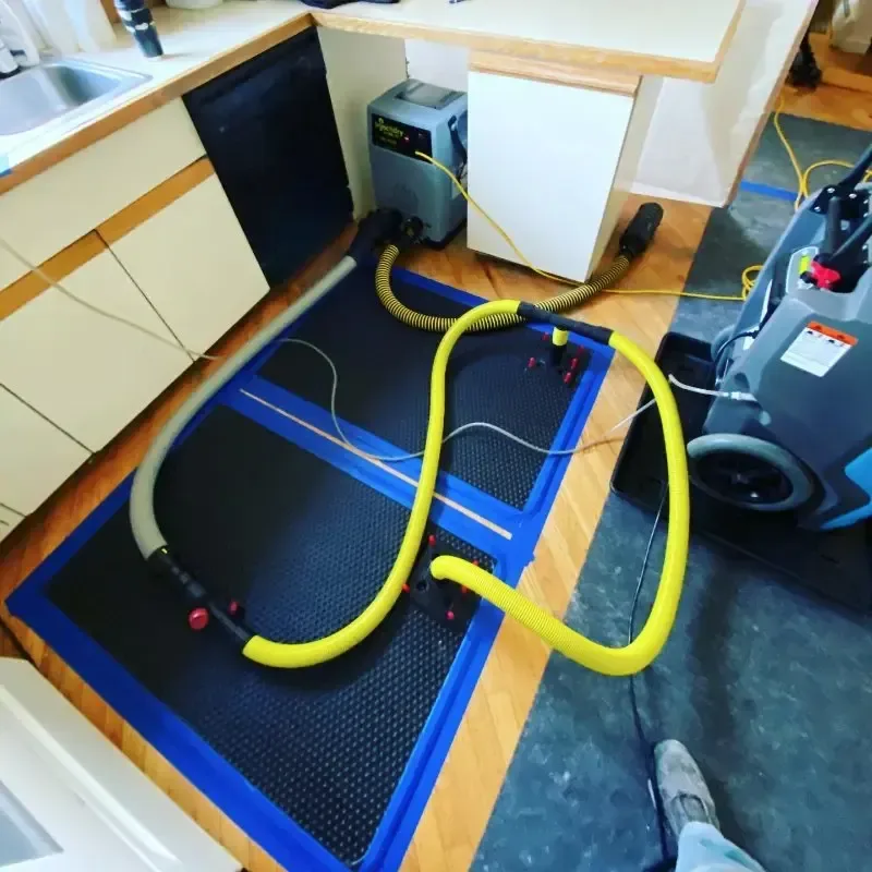 Blue floor drying mat with yellow hoses beside kitchen cabinets and a drying machine