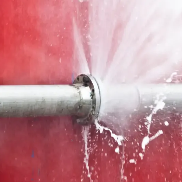 Metal pipe spraying water from a joint against a red wall during a burst pipe loss