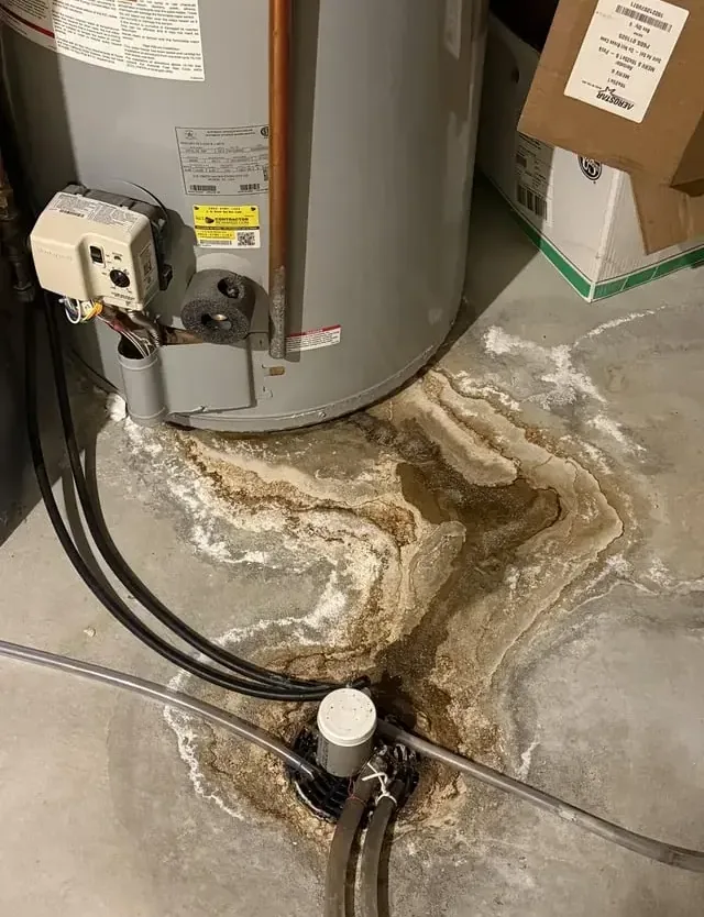 Leak stains spreading across a concrete floor around a water heater